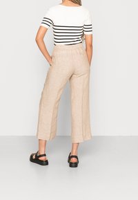 Béžové lněné kalhoty s širokými nohavicemi a kapsami, s pohodlným elastickým pasem a texturovaným povrchem. Kombinováno s černými platformovými sandály.