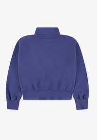 Sudadera púrpura con un alto cuello, dobladillo acanalado y puños elásticos. Textura suave con una pequeña etiqueta en la parte posterior.