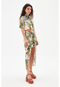 Bloemenprint, cropped button-up shirt met korte mouwen in groen en geel. Bijpassende rok met hoge split en strik in de taille. Bruine plateau sandalen.