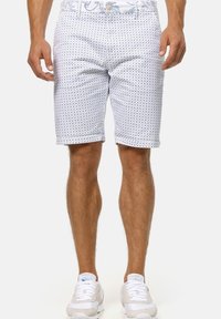 Shorts blancs avec un motif circulaire bleu, fabriqués en tissu léger, dotés d'une taille plate et d'ourlets retroussés. Portés avec des baskets blanches.