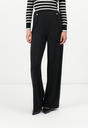 Un pantalon noir à jambes larges en tissu lisse, avec des accents de boutons dorés à la taille et une coupe ajustée.