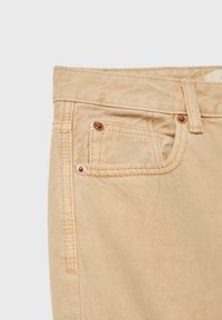Beige denimjeans har en rak klippdesign, kontrasterande sömmar och hårdvara i kopparton, inklusive en liten framficka.