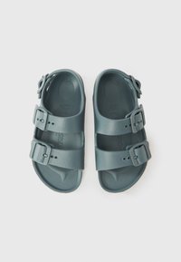 Tofargede grå sandaler med to justerbare stropper med spenner, en teksturert overflate og en formet fotseng.