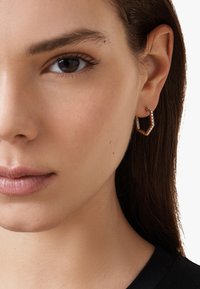 Boucle d'oreille en or avec un design géométrique, présentant une rangée de petits cristaux transparents le long d'un bord. Texture lisse et forme moderne.