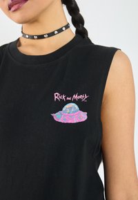 Schwarzes ärmelloses T-Shirt mit einem bunten Grafikmotiv eines UFOs mit Figuren, auf einem glatten Baumwollstoff. Chocker mit silbernen Nieten.