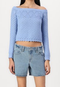 Ljusblå off-shoulder stickad tröja med ett strukturerat diamantmönster, ihopparad med denimshorts i ett blekt blått tvätt.