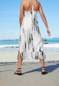 Vestido de verano en blanco y negro con rayas verticales, con un dobladillo recto y aberturas laterales. Combinado con sandalias negras de tiras.