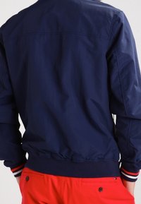 Marinblå lätt bomberjacka med ribbad krage och manschetter, elastisk midja och kontrasterande randiga detaljer på ärmarna.