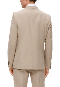 Beige Sportjacke mit glatter Textur und taillierter Passform. Mit zwei schwarzen Knöpfen an den Ärmeln und einem einzelnen Rückenventil.