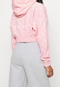 Rosa cropped Hoodie aus strukturiertem Stoff mit elastischem Saum und Bündchen. Kombiniert mit grauen Jogginghosen mit lockerem Sitz.