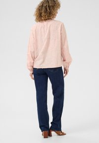 Pink embroidered blouse with long sleeves, featuring floral designs, paired with dark blue straight-leg jeans and brown heeled sandals.