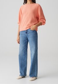 Pullover a trama corallo con maniche a tre quarti, abbinato a jeans a gamba larga blu chiaro e scarpe slip-on beige.