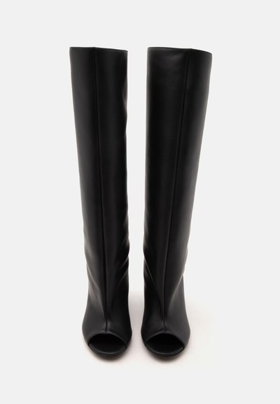 Paire de bottes hautes en cuir noir avec bouts ouverts, montrées debout sur un fond clair.