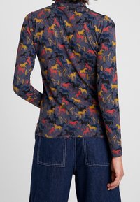 Långärmad topp i mörkt tyg med ett flerfärgat hästmönster (röd, gul, svart) och slät textur.