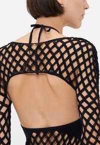 Top in maglia nera con schiena aperta, maniche lunghe decorate con un motivo a rombi e chiusura con lacci al collo. Design testurizzato e trasparente.