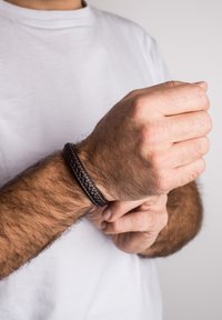Brățară din piele împletită de culoare maro închis pe un încheietură, textură netedă, formă circulară, potrivită strâns împotriva pielii, design minimalist.