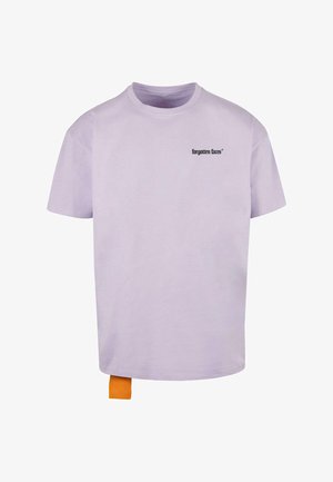 Gaiši purpursarkans kokvilnas T-krekls ar apaļu kaklu, kas ir ar melnu drukātu logotipu "aizmirstie sejiņas" un mazu oranžu auduma birku apakšmalā.