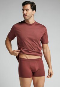 Bordowa bawełniana koszulka z okrągłym dekoltem i dopasowane bokserki. Miękka tekstura, dopasowany krój i krótkie rękawy. Widoczne minimalistyczne detale marki.