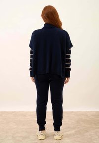 Granatowy, oversize sweter z wysokim kołnierzem i paskowanymi rękawami. Miękka tekstura, w zestawie z dopasowanymi granatowymi spodniami i jasnymi trampkami.