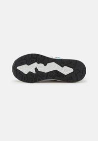 Semelle en caoutchouc robuste noire et blanche d'une chaussure de sport avec des crampons à motifs et le nom de la marque embossé au centre.