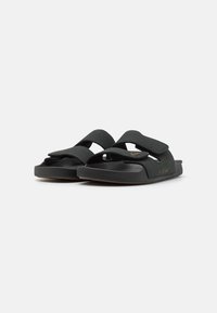 Sandales noires avec deux brides réglables, un design à bout arrondi et une semelle intérieure texturée. Fabriquées en matériau doux avec une semelle légère.