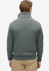 Sudadera gris con cuello alto, puños y cintura acanalados. Textura suave, diseño sencillo, sin patrones visibles ni detalles de hardware.