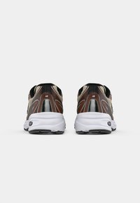Chaussures de sport brunes et noires avec une tige en mesh texturé, semelle intermédiaire blanche et semelle extérieure noire, présentant des accents argentés et un détail réfléchissant.