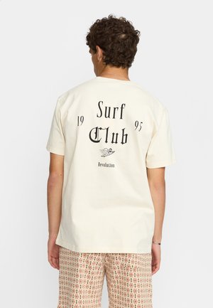Camiseta de algodón crema con el texto negro "Surf Club 1995" y una ilustración en la parte posterior. Mangas cortas, corte relajado.