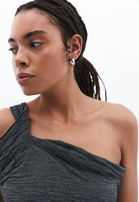 En axelbandslös topp i glittrande svart tyg med texturerade veck och en slät yta. Ett silverfärgat hoop-örhänge ger en metallisk accent.