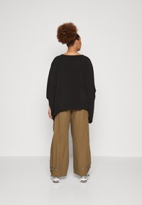 Black, loose-fitting top with a wide neckline, paired with beige wide-leg pants featuring side pockets and cuff details. Silver sneakers complete the look.