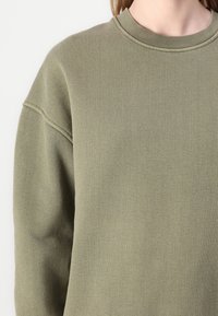 Olijfgroene sweatshirt met een ronde halslijn en geribde manchetten. Heeft een zachte, gestructureerde stof en een relaxte, oversized pasvorm.