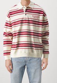 Polohemd in Creme mit roten und schwarzen horizontalen Streifen, mit Kragen, einer Drei-Knopf-Leiste und besticktem Logo auf der Brust.