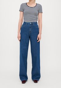 Pasiasta granatowo-biała koszula z krótkim rękawem w połączeniu z wysokim stanem, szerokimi niebieskimi dżinsami. Gładka tekstura, klasyczny krój.