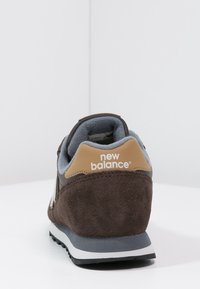 Baskets de sport en suède marron de New Balance, avec un panneau gris, un accent tan sur le talon et un col rembourré. Semelle en caoutchouc noire.