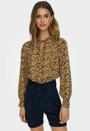Bruine bloempatronen blouse met lange mouwen en strikkoord detail, gecombineerd met hoogzitende marineblauwe shorts. Zachte stof met een gestructureerde uitstraling.