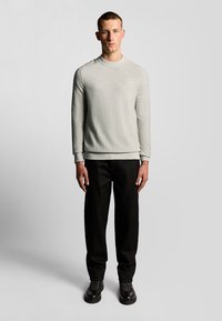 Lichtgrijze longsleeve sweatshirt met een ronde hals, gecombineerd met zwarte rechte broek en zwarte veterschoenen. Gladde textuur, minimalistisch ontwerp.