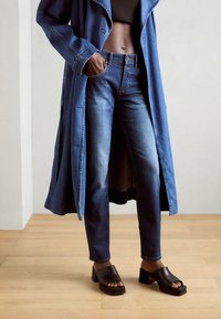 Abrigo largo de denim, vaqueros skinny de color azul oscuro y plataformas negras de punta abierta. Características: textura suave, cierre de botón y tacones gruesos.