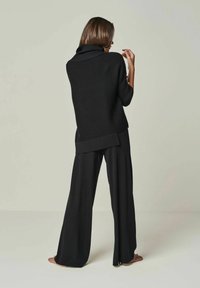 Schwarzer gerippter Pullover mit weit geschnittenem Kragen, kombiniert mit lockeren schwarzen Hosen, beide aus weichem, strukturiertem Stoff und in entspannter Passform.