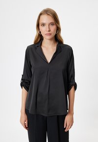Zwarte zijden blouse met een V-hals, driekwart mouwen en manchet-details. Glad textuur met een lichte plooidesign aan de voorkant.