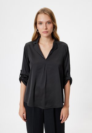 Blusa di seta nera con scollo a V, maniche tre quarti e dettagli a polsino. Tessuto liscio con un leggero design a piega frontale.