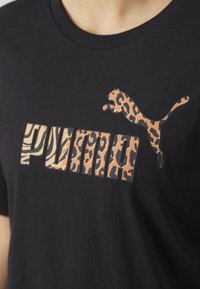 Černé bavlněné tričko s výraznou grafikou, na níž jsou vzory zvířecího tisku tvořící nápis "PUMA", vedle něhož se nachází skákající kočičí logo ve stejných barvách.