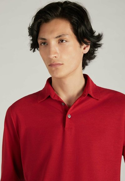 Rode polo met lange mouwen, gemaakt van zachte stof. Voorzien van een kraag met twee knopen en een subtiele textuur, wat zorgt voor een ontspannen pasvorm.