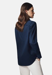 Granatowa satynowa koszula z kołnierzem, długimi rękawami i zapięciem na guziki. Charakteryzuje się gładką teksturą i lekko zaokrąglonym dołem.