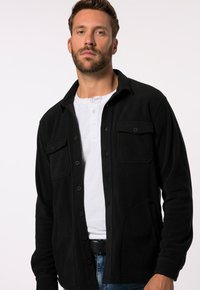 Camisa de forro polar negra con cierre de botones, dos bolsillos en el pecho y un bolsillo lateral, con una textura suave y un ajuste relajado.