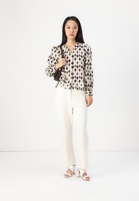 Cream blouse with dark geometric patterns, button-down style, paired with textured white trousers and white block-heel sandals.