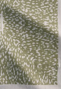 Tissu vert à motif avec un design texturé, présentant des formes blanches irrégulières sur un fond vert atténué. Les bords sont ourlés.