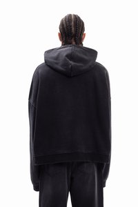 Υπερμεγέθη μαύρο φούτερ με μαλακή, υφή που θυμίζει ύφασμα, με κουκούλα που ρυθμίζεται με κορδόνι και χαλαρούς ώμους. Συνδυάζεται με αντίστοιχο σκούρο παντελόνι.