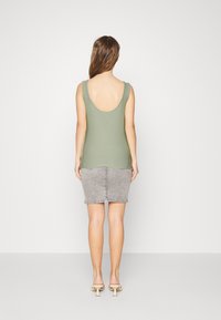 Débardeur vert olive à dos décolleté, associé à une jupe en denim grise. La tenue est complétée par des sandales à talons blancs.