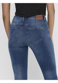 Närbild av en person som bär blå denimjeans med bakfickor och en brun läderlapp märkta "ONLY" på midjan.