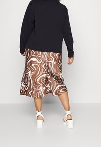 Falda midi de estampado marrón y blanco con dobladillo acampanado, combinada con un sudadera negra y tacones gruesos blancos. Tejido suave y corte holgado.